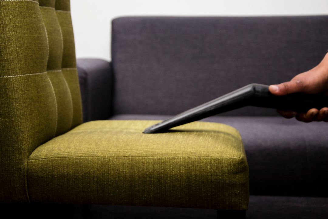 Main passant un aspirateur textile sur un fauteuil en tissu vert