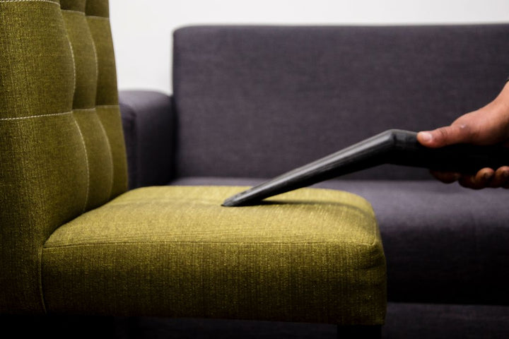 Main passant un aspirateur textile sur un fauteuil en tissu vert
